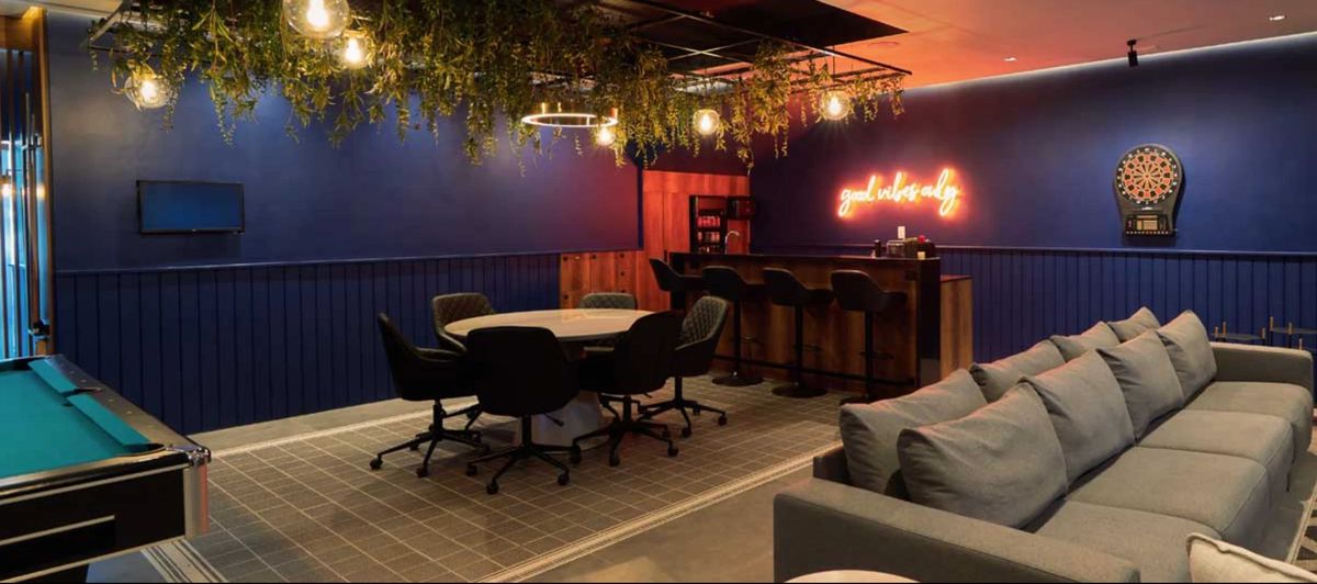 Sala de The Lounge Marbella: paredes azules, letrero de neón, mesa de billar y diana de dardos