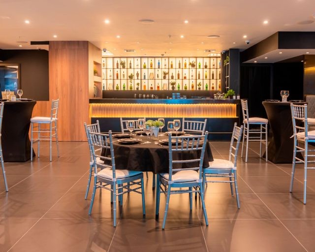 Sala de The Lounge San Francisco: mesa de banquete montada, mesas altas y barra iluminada